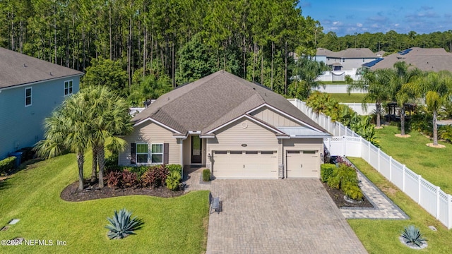 view of front of property with a garage, decorative driveway, a fenced backyard, and a front lawn