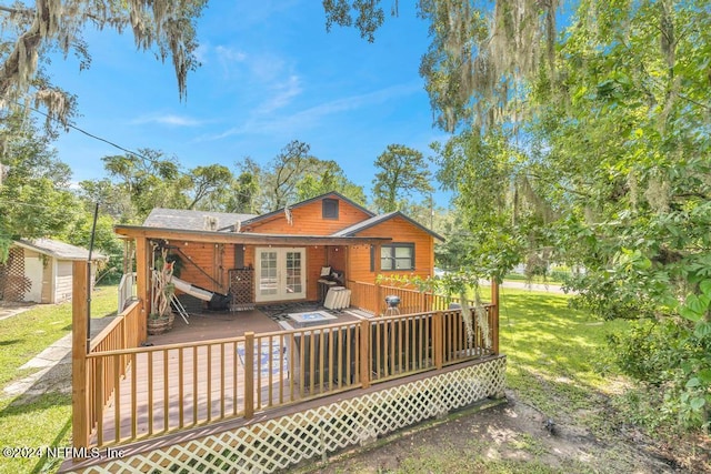 rear view of house featuring a yard, a wooden deck, french doors, and a storage unit