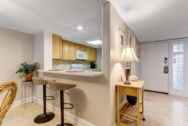 kitchen with a textured ceiling, white appliances, a breakfast bar, light countertops, and decorative backsplash