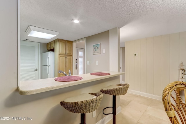 kitchen featuring light countertops, freestanding refrigerator, a textured ceiling, a peninsula, and a kitchen bar