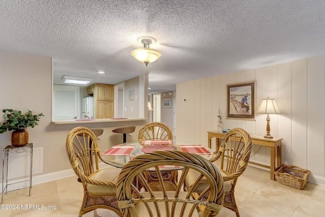 dining area with light tile patterned flooring, a textured ceiling, and baseboards