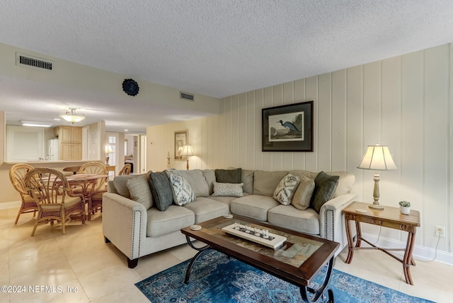 living room featuring light tile patterned floors, baseboards, visible vents, and a textured ceiling