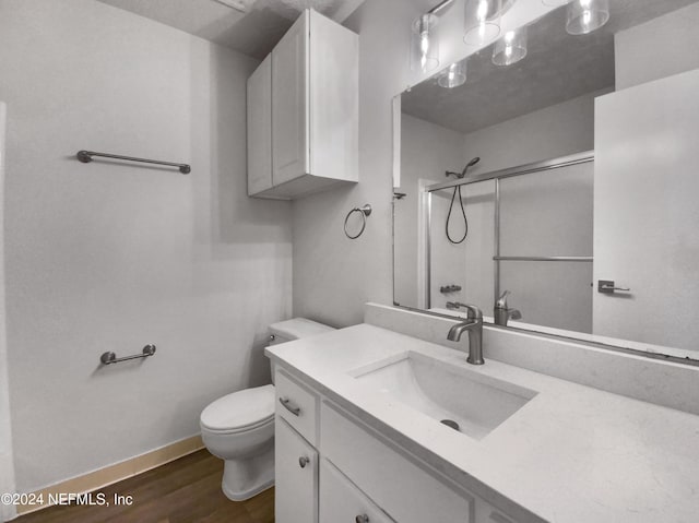 bathroom featuring a shower with door, toilet, vanity, wood finished floors, and baseboards