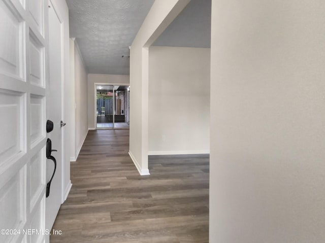 corridor with dark wood finished floors, a textured ceiling, and baseboards