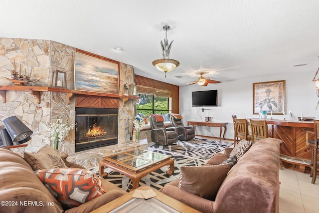 living area with a textured ceiling, a fireplace, light tile patterned flooring, and a ceiling fan