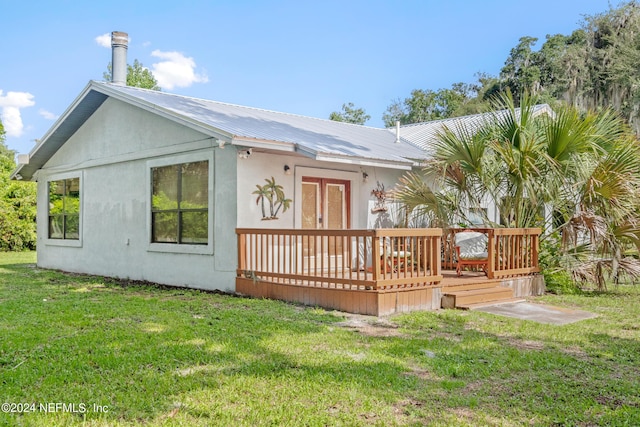 back of house featuring metal roof, a yard, a deck, and stucco siding