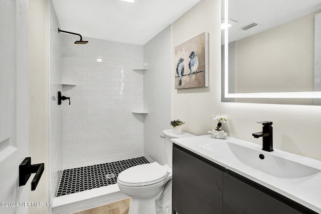 bathroom with tiled shower, vanity, and toilet