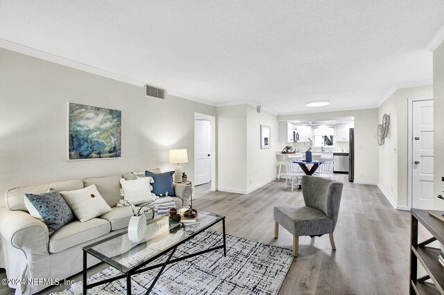 living room with a textured ceiling, light hardwood / wood-style flooring, and ornamental molding