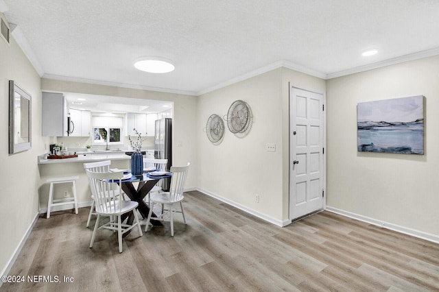 dining room with light wood-type flooring, ornamental molding, and a textured ceiling