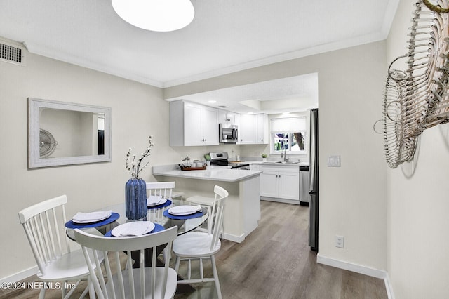 kitchen with a breakfast bar, wood-type flooring, kitchen peninsula, stainless steel appliances, and white cabinets