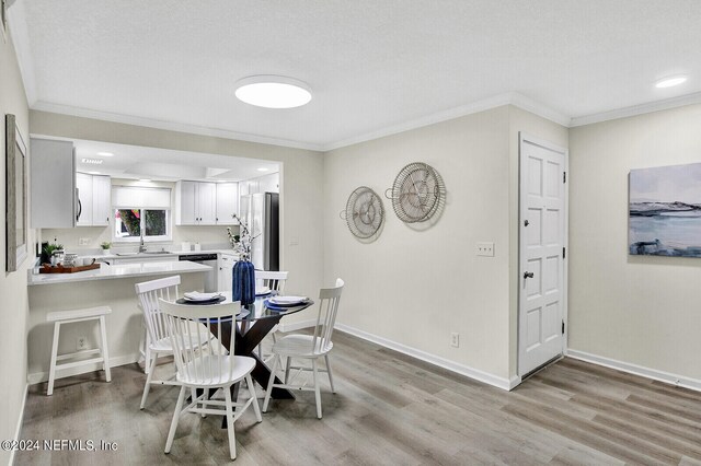 dining room featuring crown molding, a textured ceiling, and light hardwood / wood-style flooring