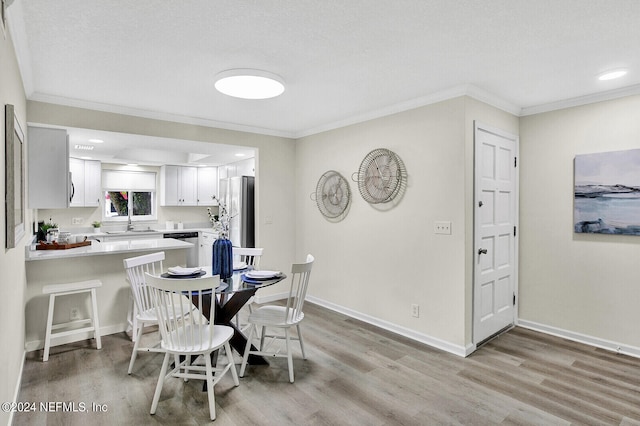 dining space with crown molding, sink, and light hardwood / wood-style floors