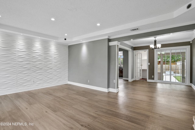 unfurnished living room with wood-type flooring, a tray ceiling, ornamental molding, and a chandelier