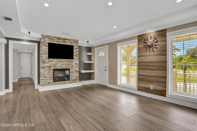 unfurnished living room with a textured ceiling, hardwood / wood-style floors, a stone fireplace, wooden walls, and built in features