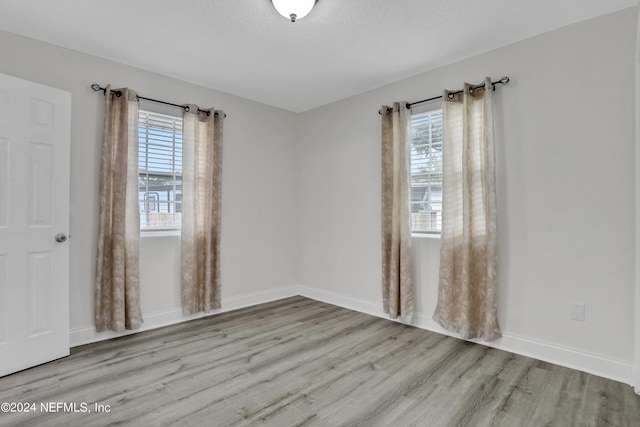 spare room with a textured ceiling, light hardwood / wood-style flooring, and a healthy amount of sunlight