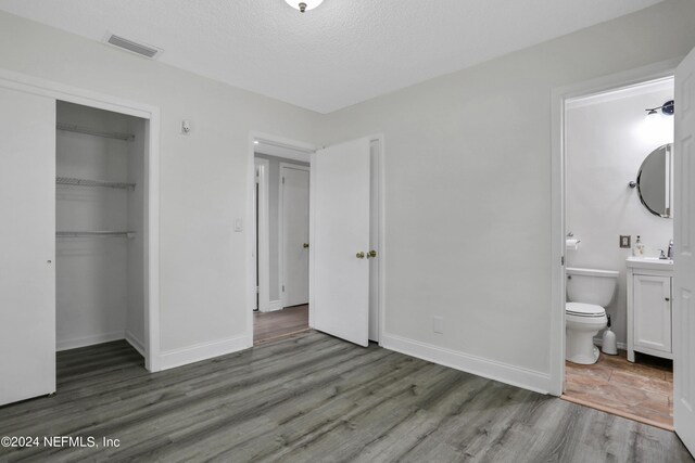 unfurnished bedroom featuring ensuite bath, dark hardwood / wood-style floors, sink, and a textured ceiling