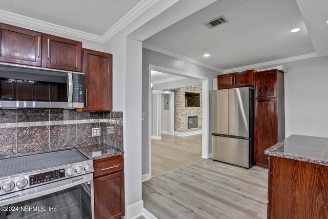 kitchen with tasteful backsplash, a fireplace, light hardwood / wood-style flooring, stainless steel appliances, and dark stone counters