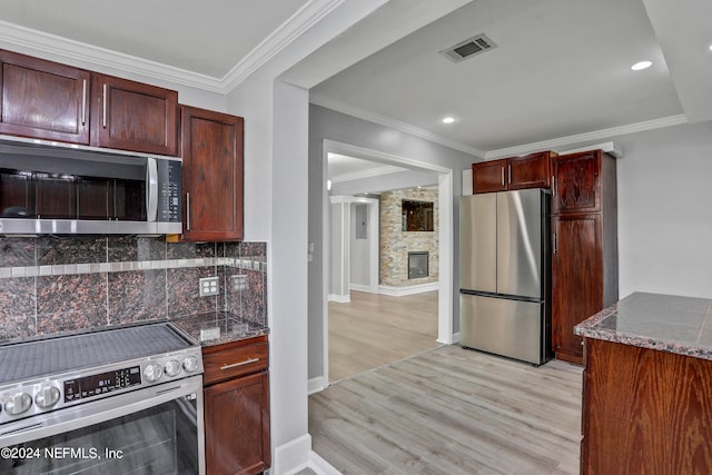 kitchen with appliances with stainless steel finishes, decorative backsplash, dark stone counters, crown molding, and light hardwood / wood-style flooring