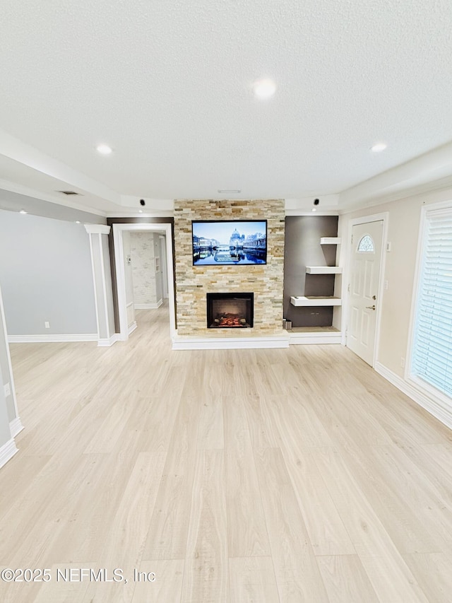 unfurnished living room featuring light hardwood / wood-style floors, a large fireplace, built in features, and a textured ceiling