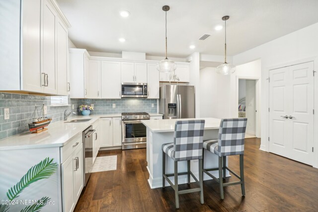 kitchen featuring tasteful backsplash, a kitchen island, dark hardwood / wood-style floors, hanging light fixtures, and appliances with stainless steel finishes