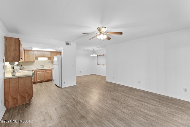 unfurnished living room with sink, ceiling fan with notable chandelier, and light hardwood / wood-style floors