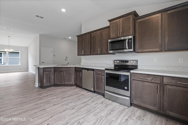 kitchen with a sink, vaulted ceiling, light countertops, appliances with stainless steel finishes, and hanging light fixtures