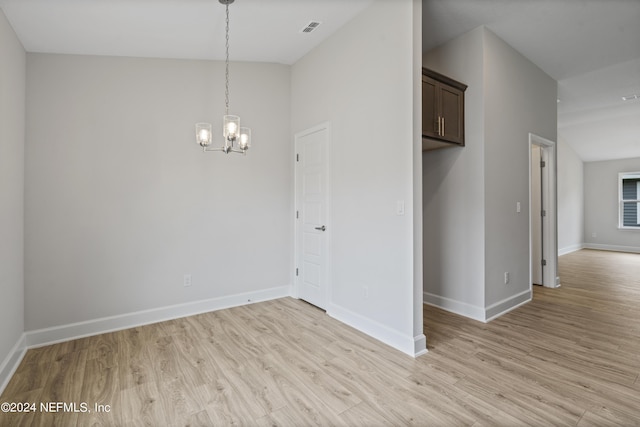 empty room with lofted ceiling, a chandelier, and light hardwood / wood-style floors