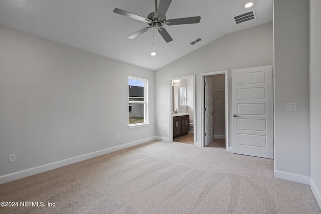 unfurnished bedroom with a spacious closet, vaulted ceiling, light colored carpet, and ensuite bathroom