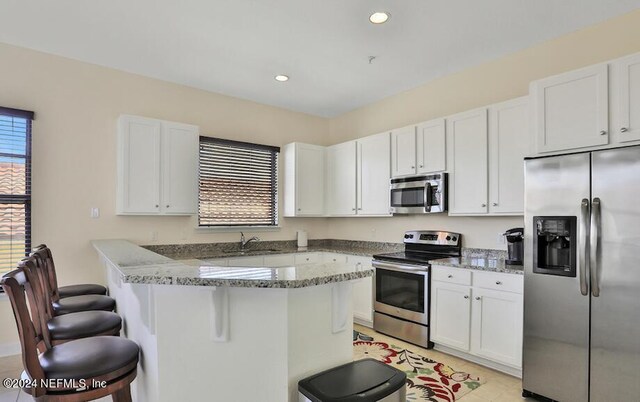 kitchen featuring white cabinetry, light stone countertops, appliances with stainless steel finishes, and a kitchen bar