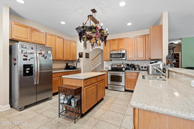 kitchen featuring light tile patterned floors, appliances with stainless steel finishes, a center island, sink, and light stone counters