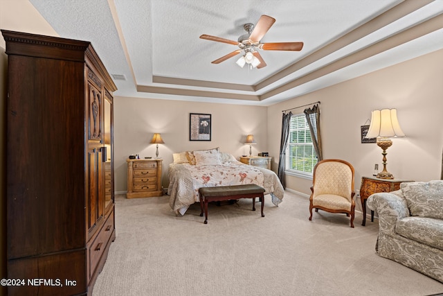 bedroom featuring a tray ceiling, light carpet, ceiling fan, and a textured ceiling