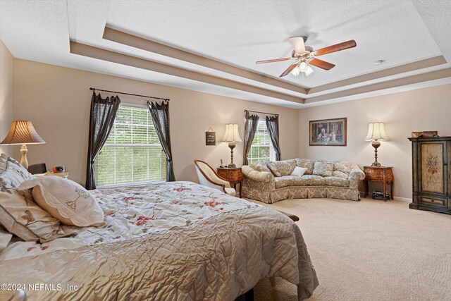 carpeted bedroom with a textured ceiling, a raised ceiling, ceiling fan, and multiple windows