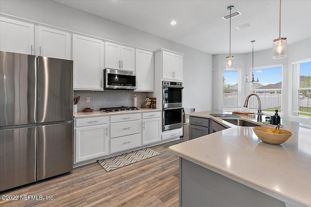 kitchen featuring white cabinetry, appliances with stainless steel finishes, decorative light fixtures, backsplash, and sink