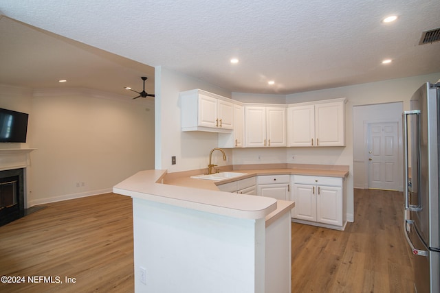 kitchen featuring light hardwood / wood-style floors, stainless steel refrigerator, white cabinets, sink, and kitchen peninsula