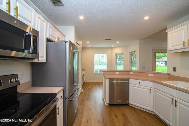 kitchen featuring a textured ceiling, appliances with stainless steel finishes, light hardwood / wood-style floors, white cabinetry, and kitchen peninsula