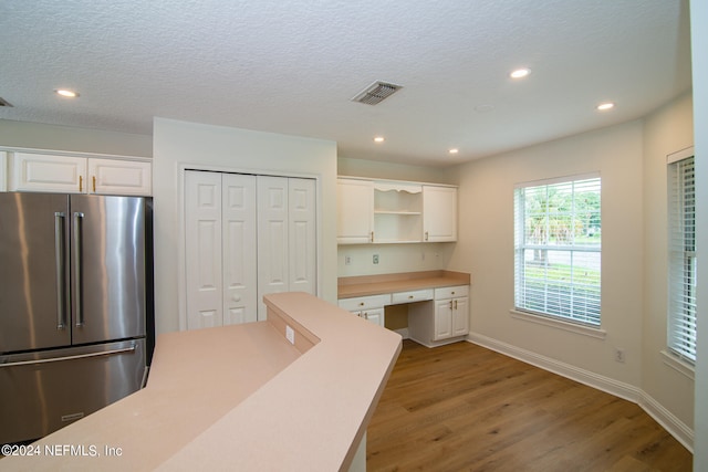 kitchen with a textured ceiling, built in desk, light hardwood / wood-style floors, white cabinetry, and stainless steel refrigerator