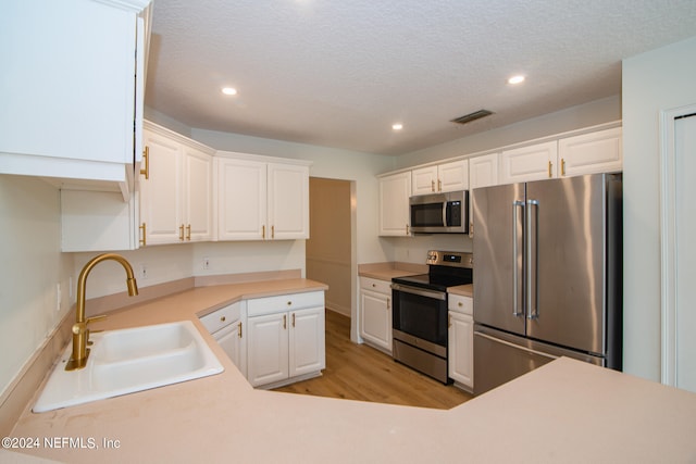 kitchen featuring light wood-type flooring, a textured ceiling, stainless steel appliances, white cabinetry, and sink