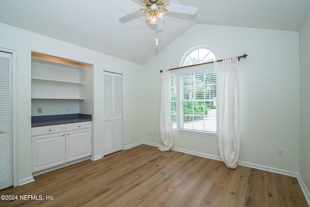 unfurnished bedroom with ceiling fan, multiple windows, light wood-type flooring, and vaulted ceiling