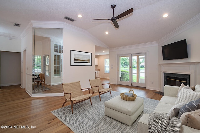 living room with a textured ceiling, a high end fireplace, ceiling fan, ornamental molding, and light hardwood / wood-style floors