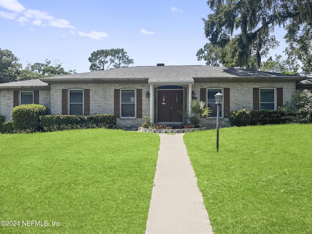 ranch-style house featuring roof with shingles, brick siding, and a front lawn