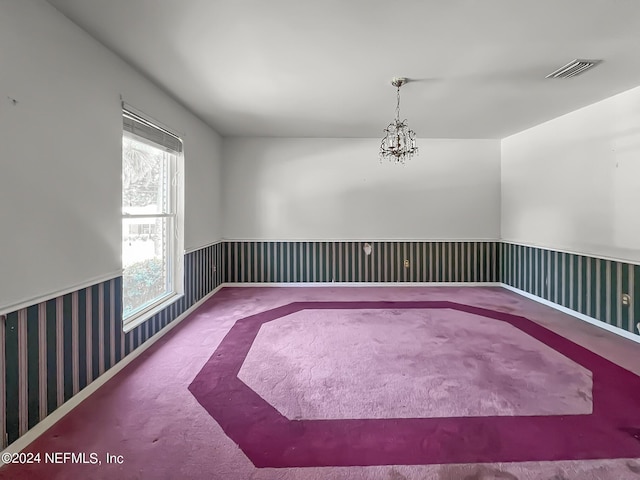 empty room featuring a wainscoted wall, carpet floors, a chandelier, and visible vents