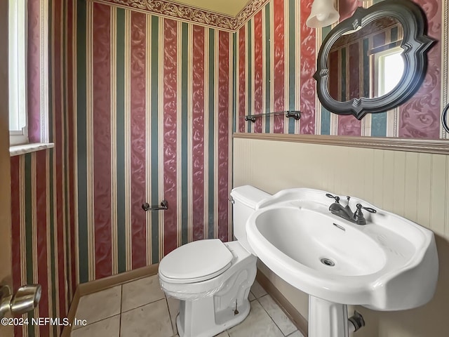 half bathroom with a wainscoted wall, a sink, toilet, and tile patterned floors