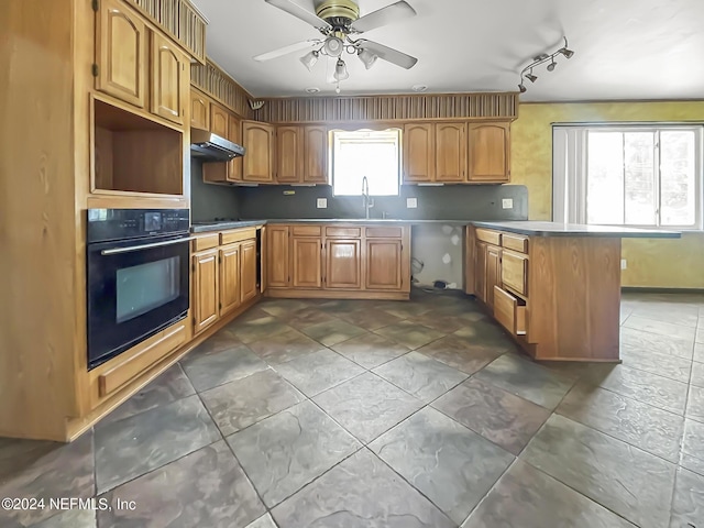 kitchen featuring under cabinet range hood, a peninsula, a sink, a ceiling fan, and black oven