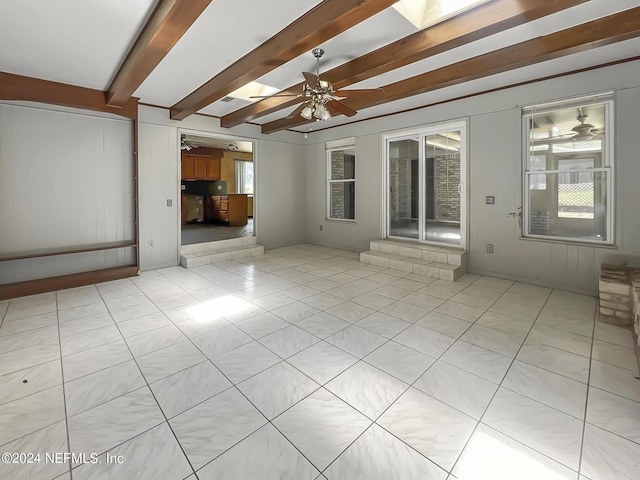 unfurnished living room featuring a ceiling fan, a skylight, beamed ceiling, and light tile patterned floors