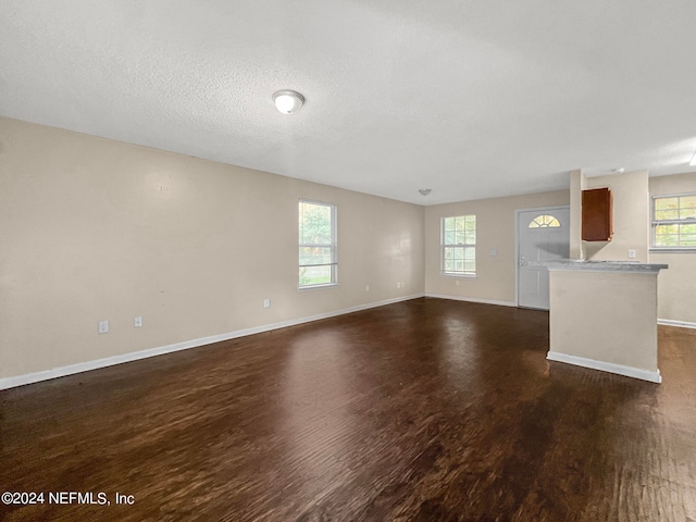 unfurnished living room with a textured ceiling, a healthy amount of sunlight, and dark hardwood / wood-style floors