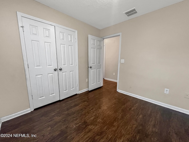 unfurnished bedroom featuring dark wood-type flooring, a closet, and a textured ceiling