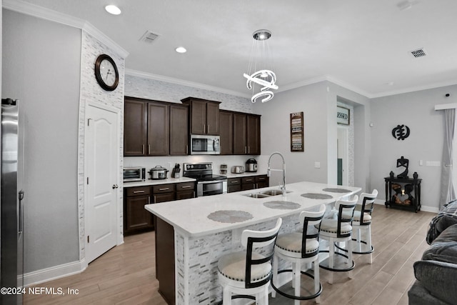 kitchen with sink, light hardwood / wood-style flooring, a kitchen island with sink, stainless steel appliances, and decorative light fixtures