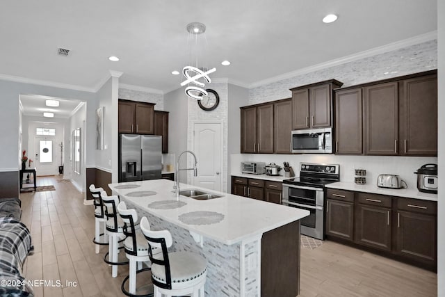 kitchen with sink, appliances with stainless steel finishes, a center island with sink, a chandelier, and light wood-type flooring