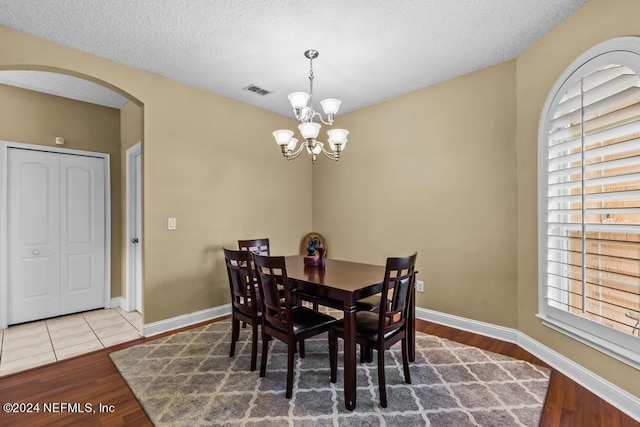 dining area with a textured ceiling, a healthy amount of sunlight, a notable chandelier, and hardwood / wood-style floors