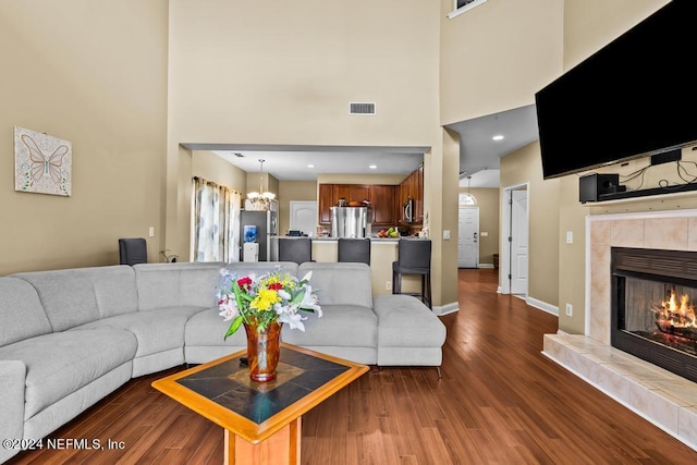 living room with dark wood-type flooring, a fireplace, a chandelier, and a towering ceiling